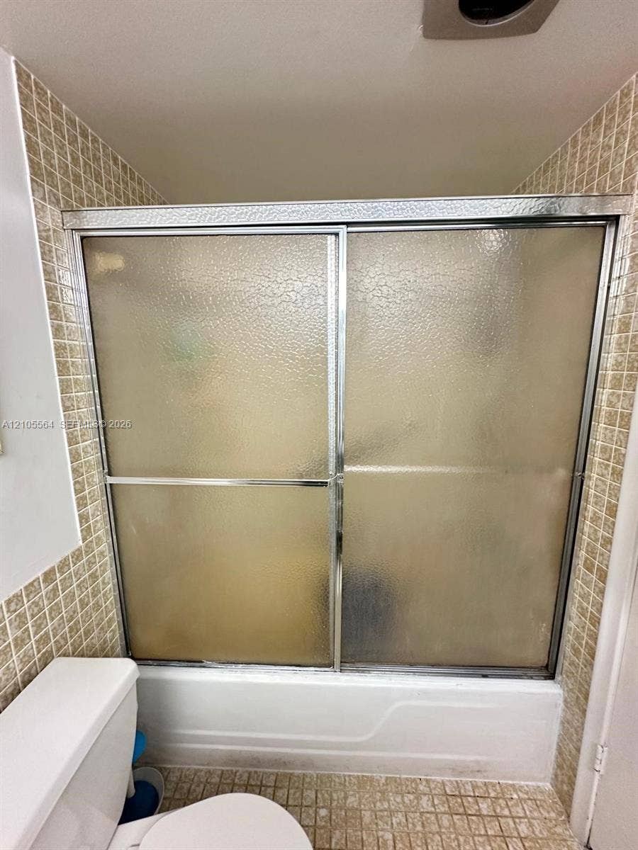 Bathtub with sliding shower doors, textured glass panels, and chrome framing