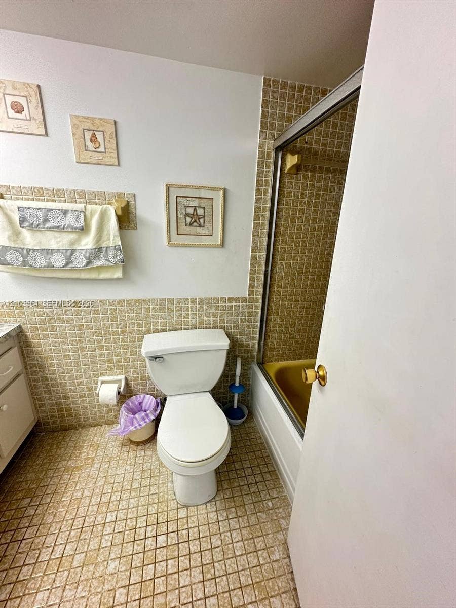 Bathroom featuring a built-in bathtub with a sliding glass enclosure, mosaic tile flooring, and mosaic wall tiling
