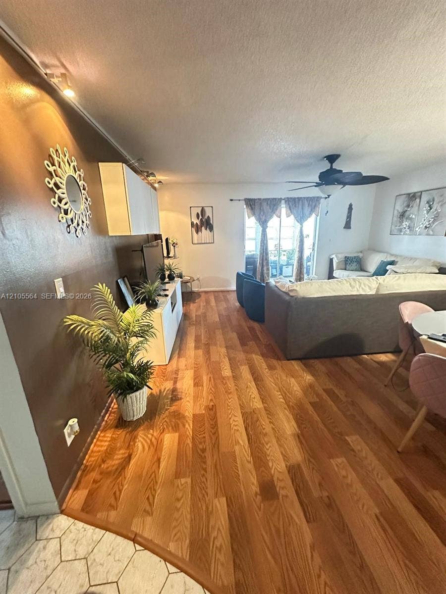 Wood-finish flooring throughout, featuring a ceiling fan, track lighting, and a window with curtains