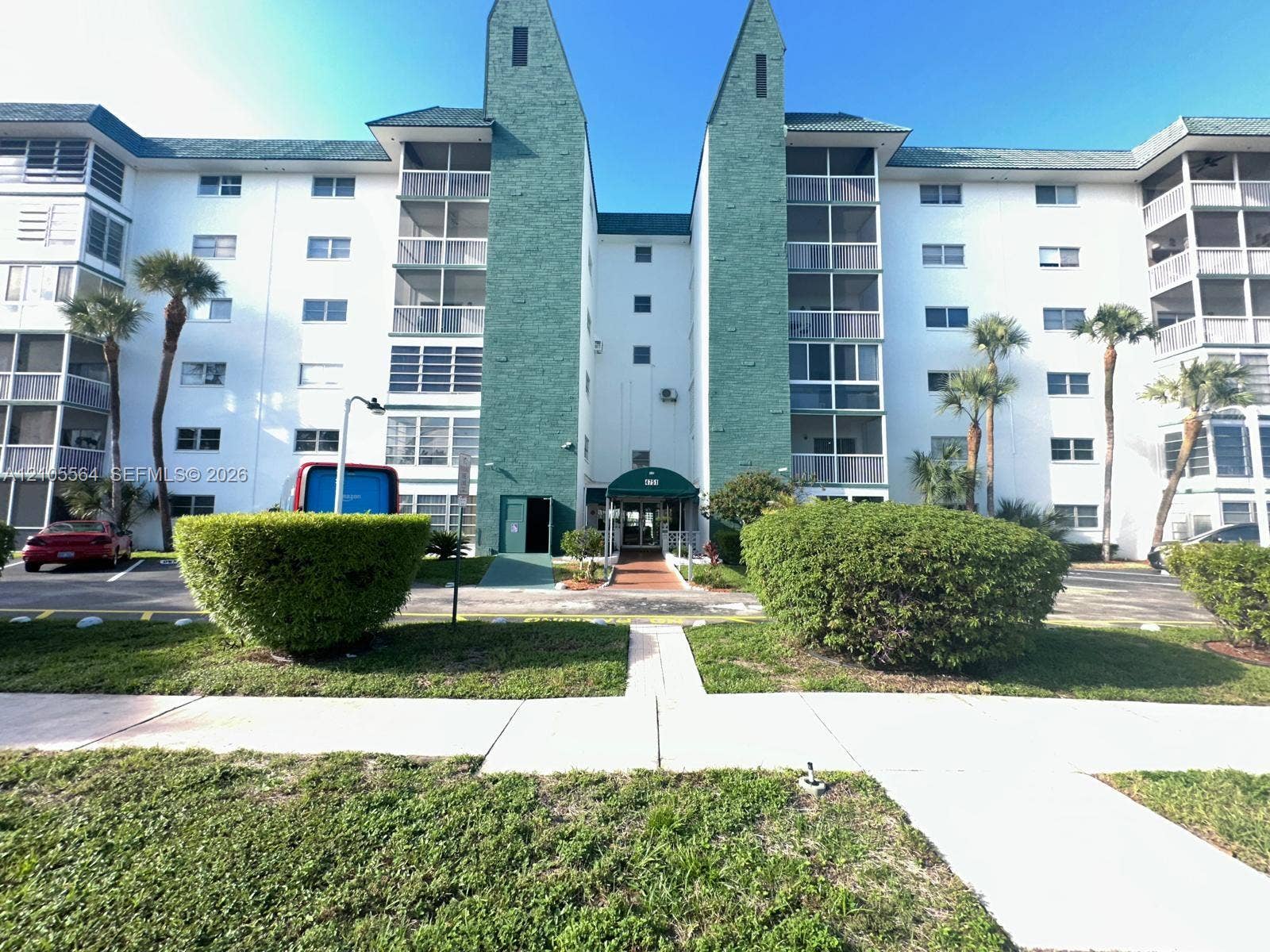 Multi-story building featuring screened balconies, a central covered entry, and manicured landscaping