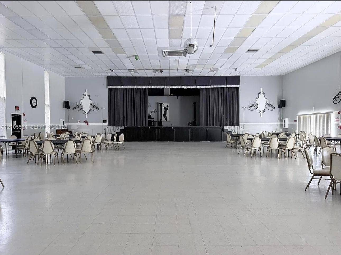 Spacious open room with a large stage, featuring dark curtains and a decorative balustrade