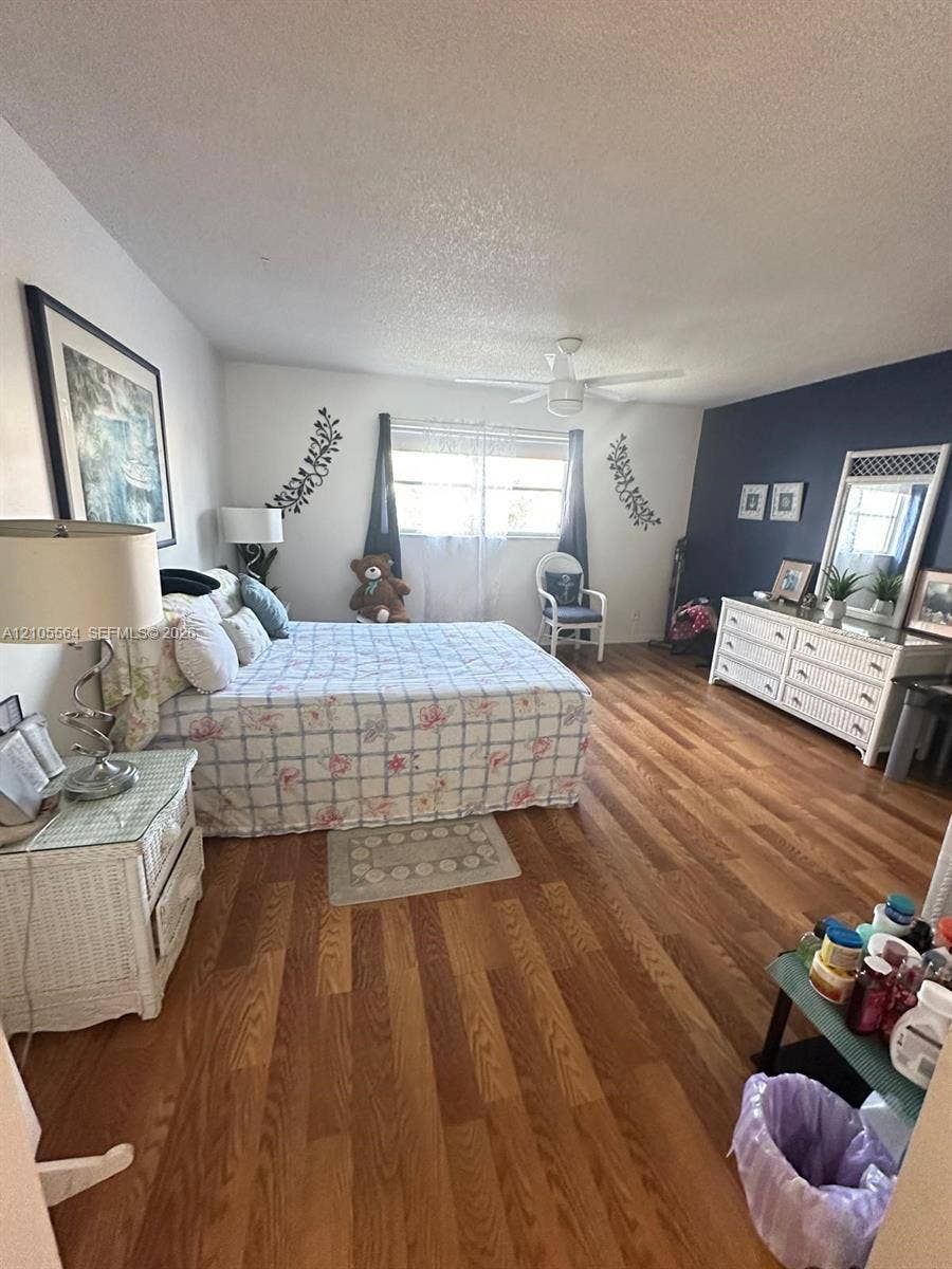 Wood-finish flooring throughout, complemented by a window with blinds, and a ceiling fan light fixture