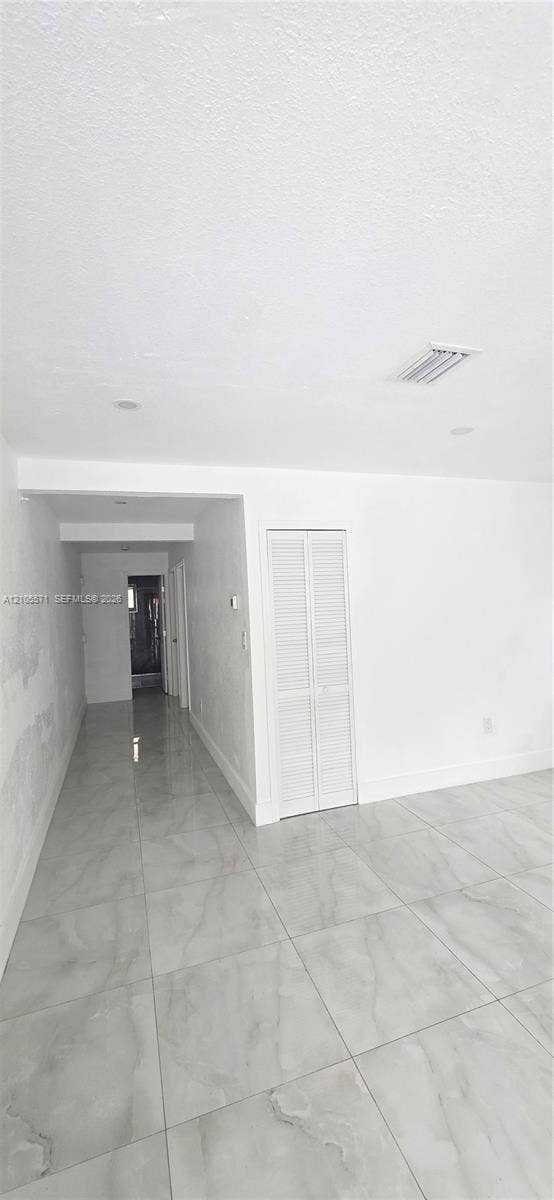 Recessed ceiling lighting with a white textured ceiling, light-toned tile flooring, and white bifold closet doors