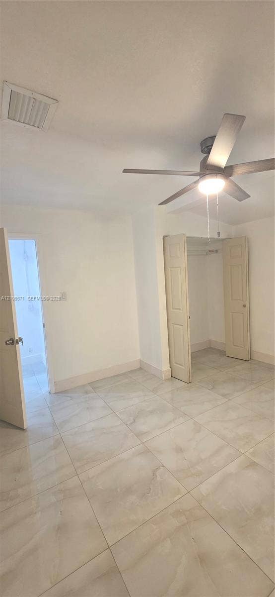 Neutral white walls, ceiling fan with integrated lighting, bi-fold closet doors, and large format floor tiling