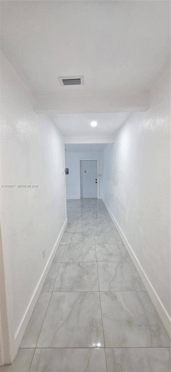 Recessed lighting illuminates the hallway, featuring light-toned tile flooring and white baseboards