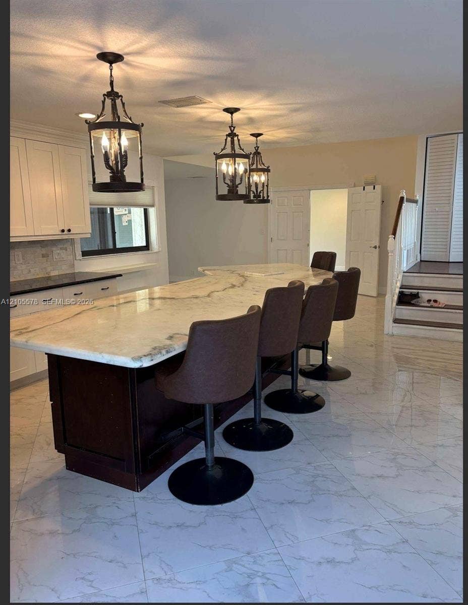 Kitchen featuring a large central island with stone-surface countertop, dark-finish cabinetry, ornate hanging pendant lighting, and polished stone-finish flooring