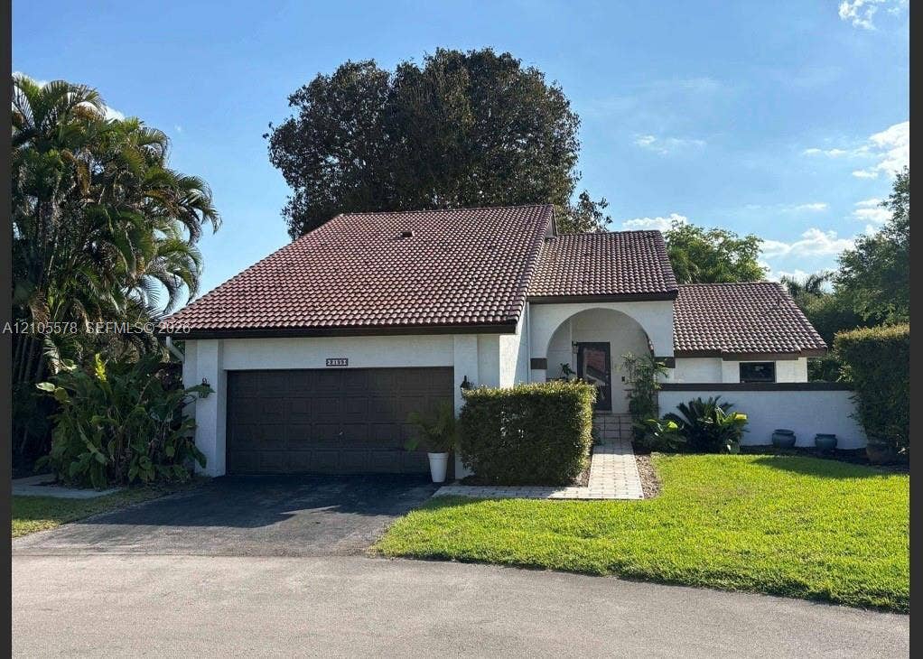 Stucco exterior residence featuring a multi-gabled tile roof, an arched covered entryway, and a paved walkway