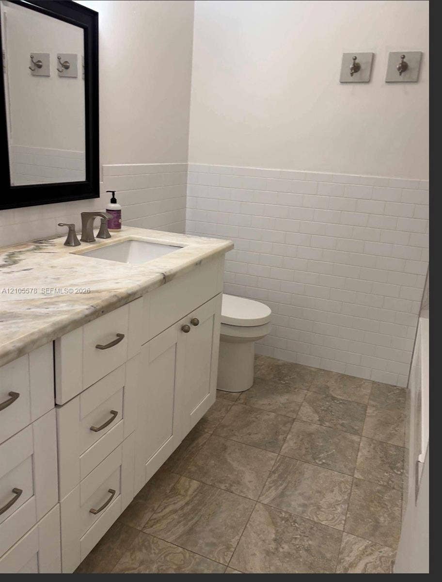 White vanity with a stone countertop, under-mount sink, subway tile wainscoting, and large-format tile flooring