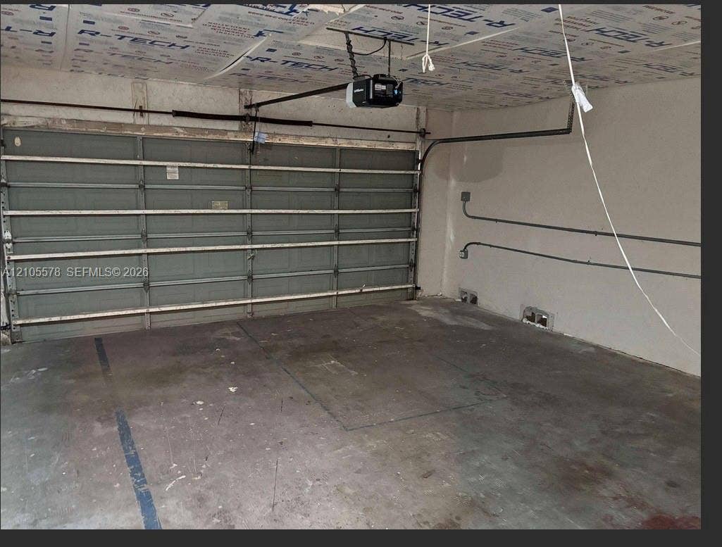 Multi-car garage featuring a sectional overhead door, automated door opener, and exposed interior wall conduit