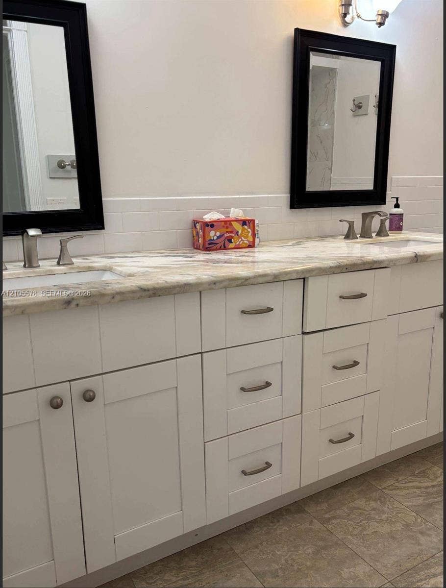 Dual-vanity bathroom featuring a light-toned stone countertop, white shaker-style cabinetry, undermount sinks, and dual black-framed wall mirrors