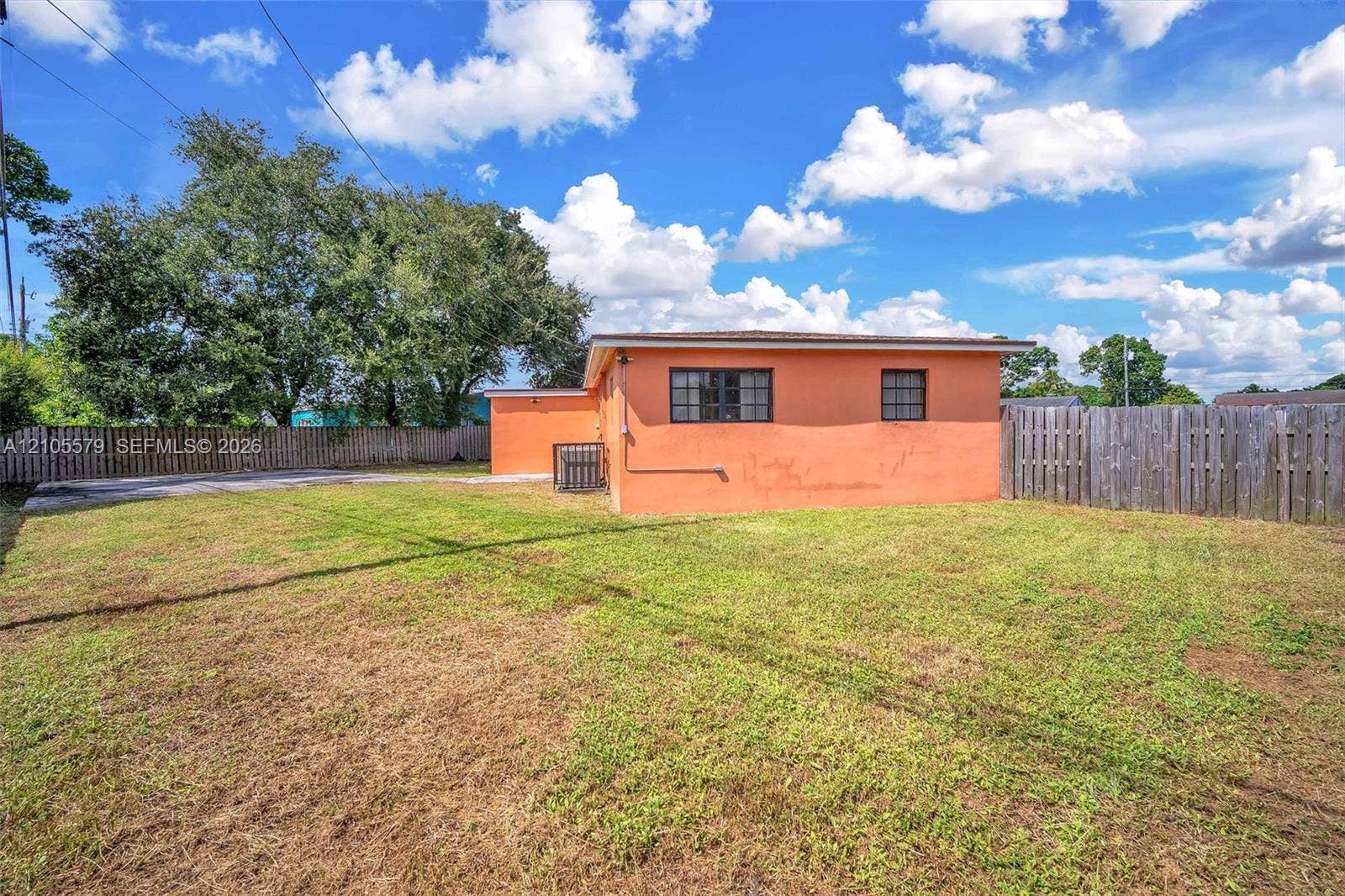 1750 NW 185th Street, Miami Gardens, FL 33056 Exterior of the residence featuring a concrete masonry unit wall finish, rectangular grid windows, and an expansive rear yard enclosed by wooden perimeter fencing