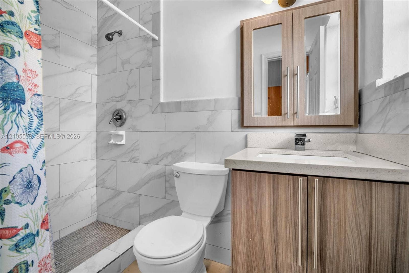1750 NW 185th Street, Miami Gardens, FL 33056 Bathroom featuring a vanity with a light-toned countertop, wood-finish cabinetry, a mirrored medicine cabinet, and a walk-in shower with large-format stone-patterned wall tile