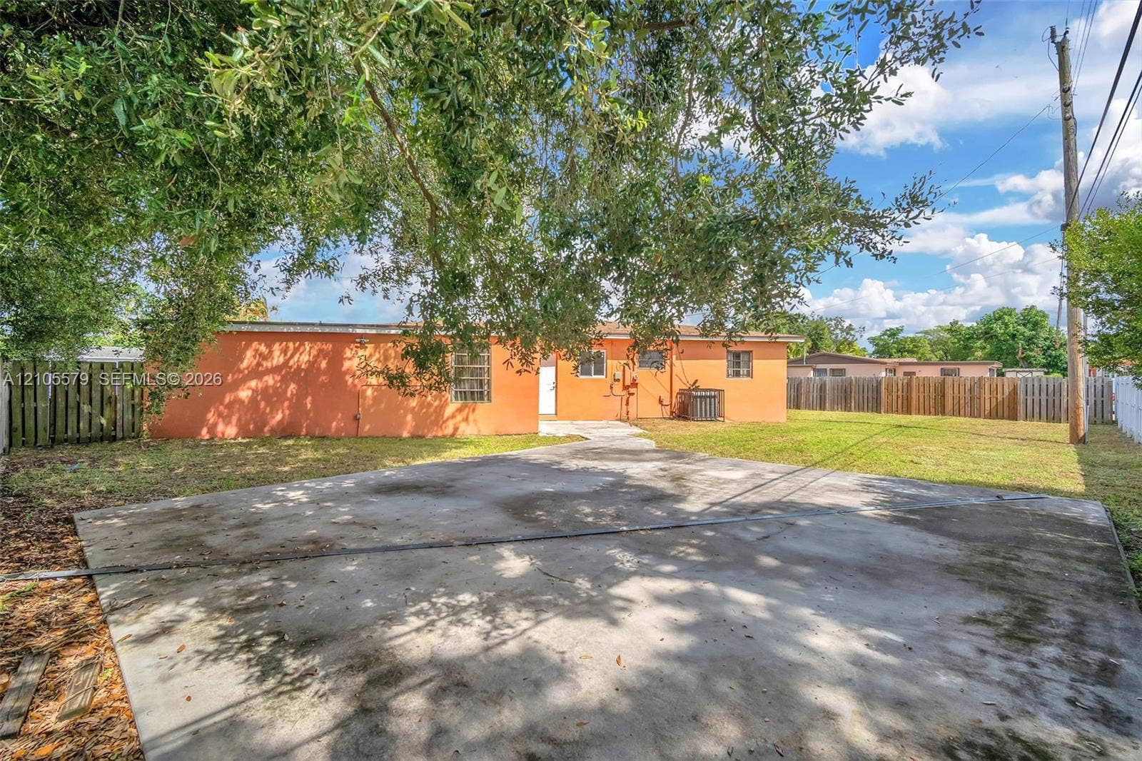 1750 NW 185th Street, Miami Gardens, FL 33056 Stucco exterior featuring a concrete driveway, fenced perimeter, and mature canopy trees