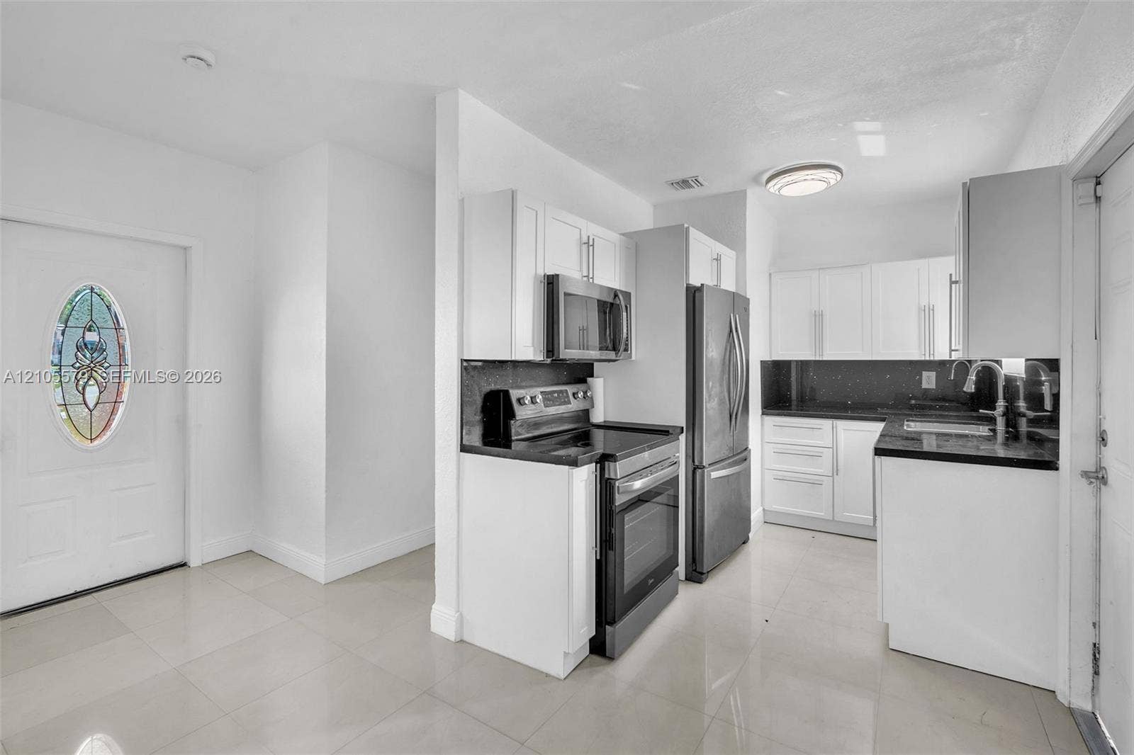 1750 NW 185th Street, Miami Gardens, FL 33056 Kitchen featuring white shaker-style cabinetry, stainless steel appliances, dark countertops, tile flooring, and a door with a decorative oval glass insert
