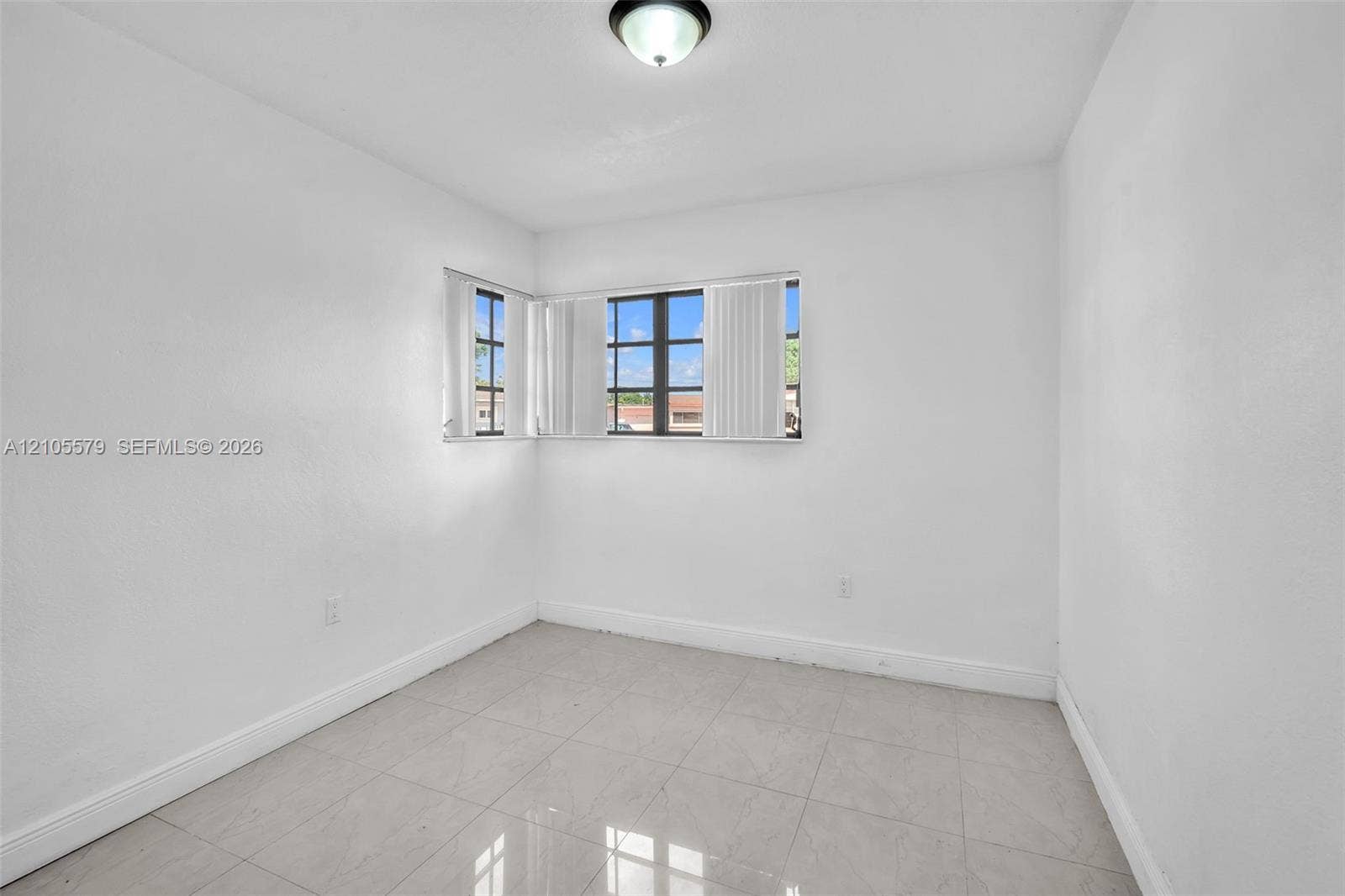 1750 NW 185th Street, Miami Gardens, FL 33056 Neutral interior space featuring polished tile flooring, smooth white walls, corner-positioned multi-pane windows, and a flush-mount ceiling fixture