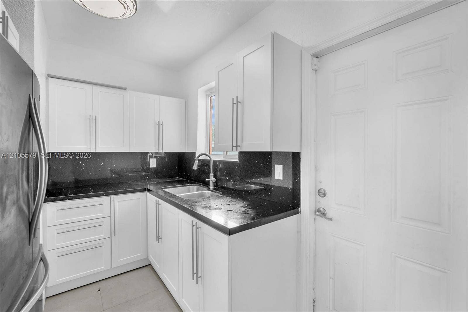 1750 NW 185th Street, Miami Gardens, FL 33056 Kitchen featuring white shaker-style cabinetry, dark stone-finish countertops, stainless steel dual-basin sink with pull-down faucet, and sleek metallic hardware