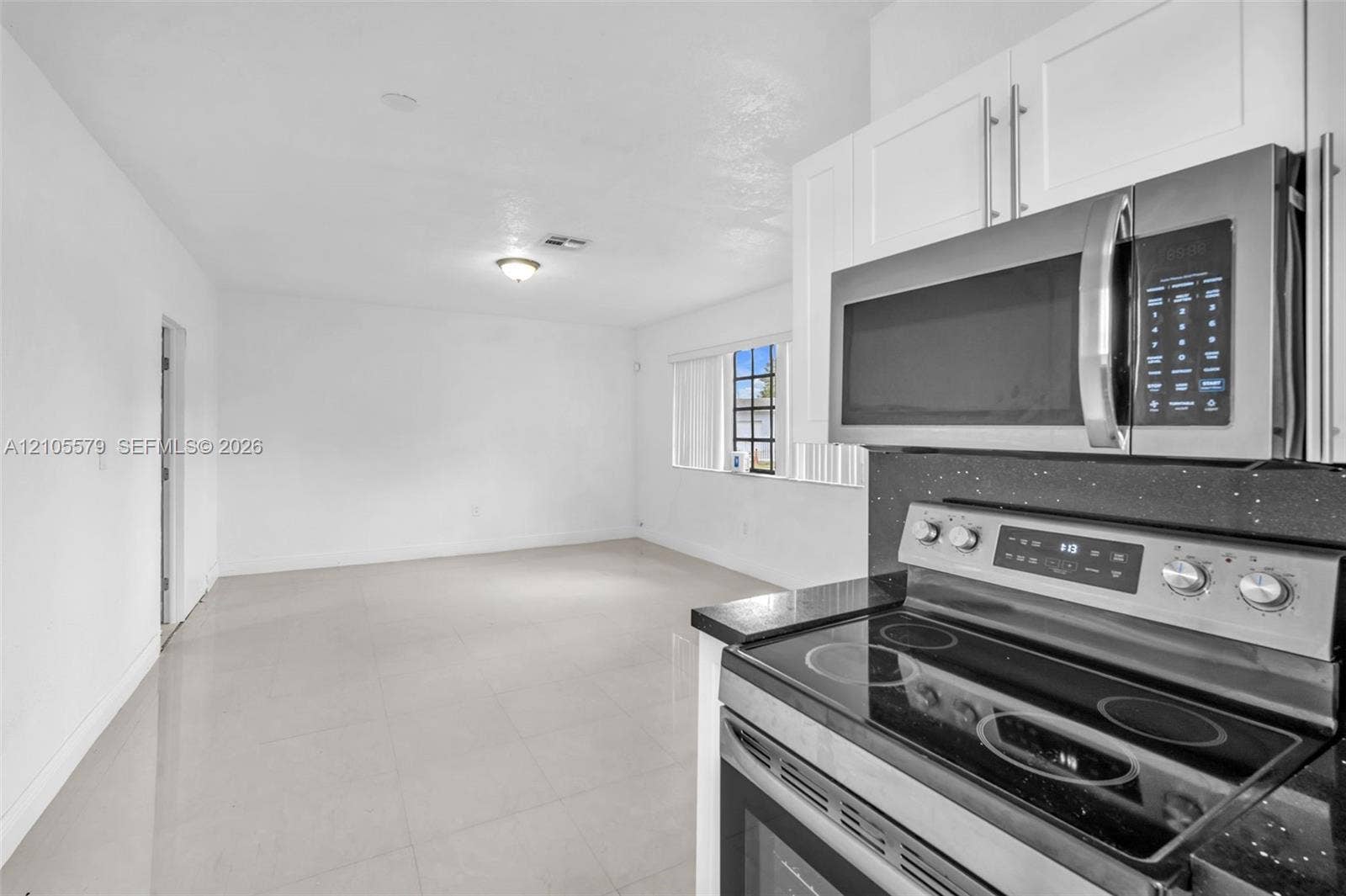 1750 NW 185th Street, Miami Gardens, FL 33056 Kitchen featuring white shaker-style cabinetry, a stainless steel microwave, and a glass-top electric range with a dark solid-surface countertop