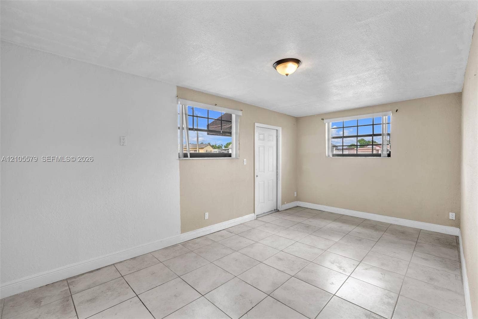 1750 NW 185th Street, Miami Gardens, FL 33056 Neutral-toned interior space featuring large-format ceramic tile flooring, two multi-pane windows with hardware, and a single-panel interior door