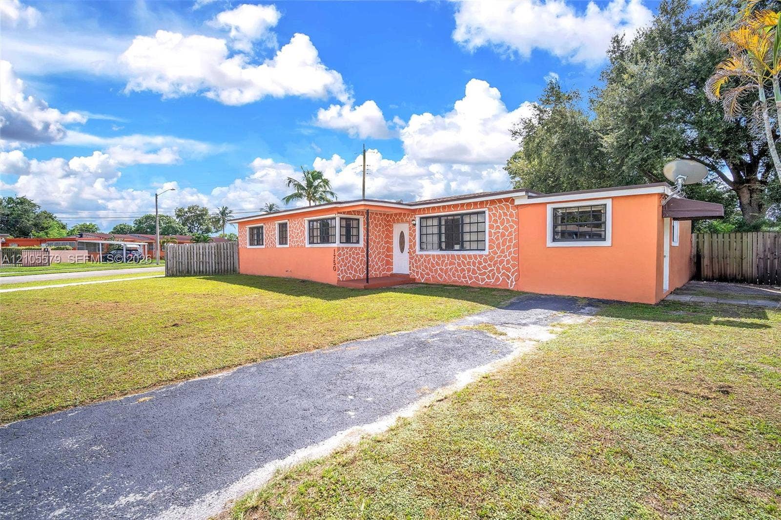 1750 NW 185th Street, Miami Gardens, FL 33056 Single-story exterior featuring a paved driveway, exterior stone veneer accents, multi-pane windows, and a fenced yard
