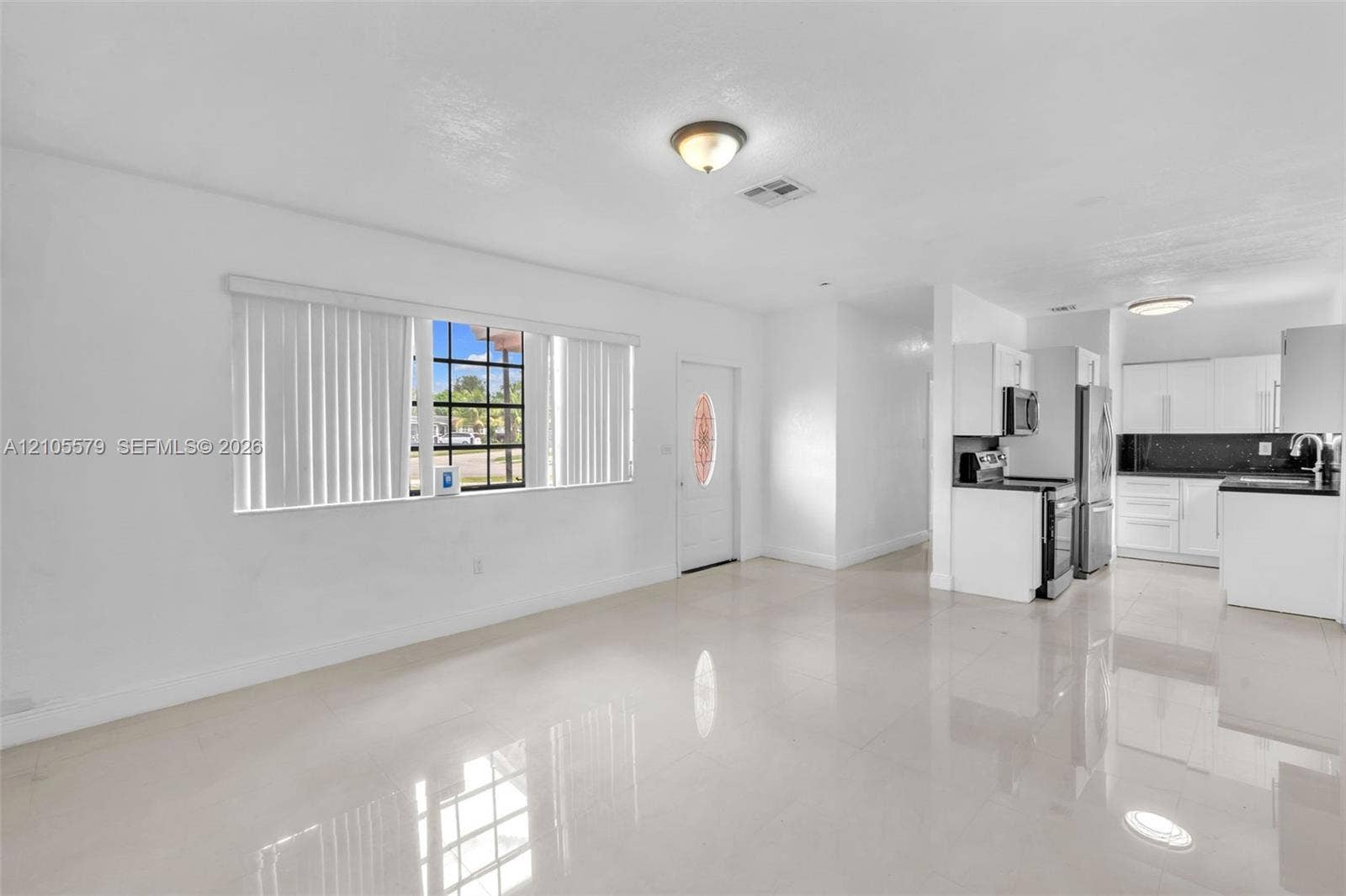 1750 NW 185th Street, Miami Gardens, FL 33056 Open floor plan featuring polished tile flooring, recessed and flush-mount ceiling lighting, window with vertical blinds, and a kitchen equipped with white cabinetry and dark countertops