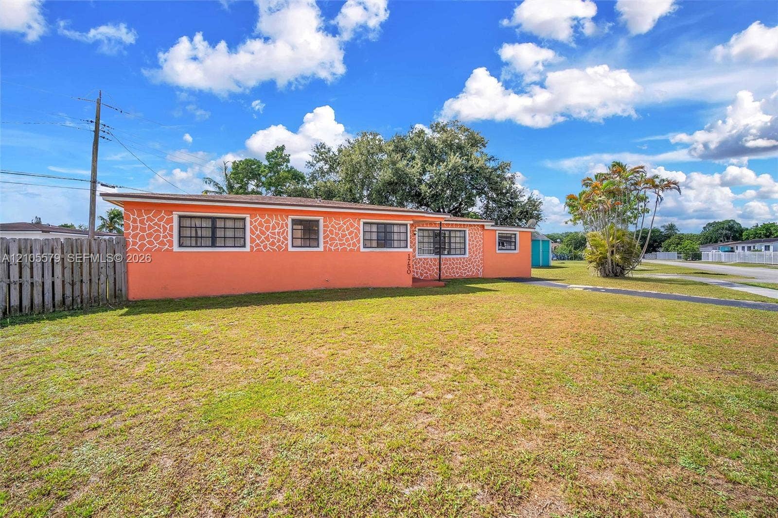 1750 NW 185th Street, Miami Gardens, FL 33056 Single-story residence featuring a distinctive orange exterior finish, decorative masonry detailing, multi-pane windows, and an expansive lawn