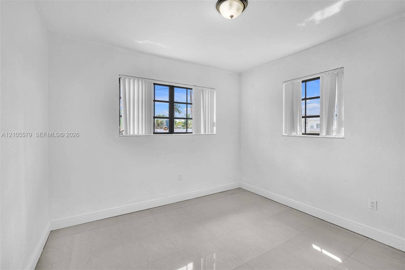1750 NW 185th Street, Miami Gardens, FL 33056 Interior space featuring large-format ceramic tile flooring, neutral wall finishes, two multi-pane windows with dark frames, and a central ceiling-mounted dome fixture