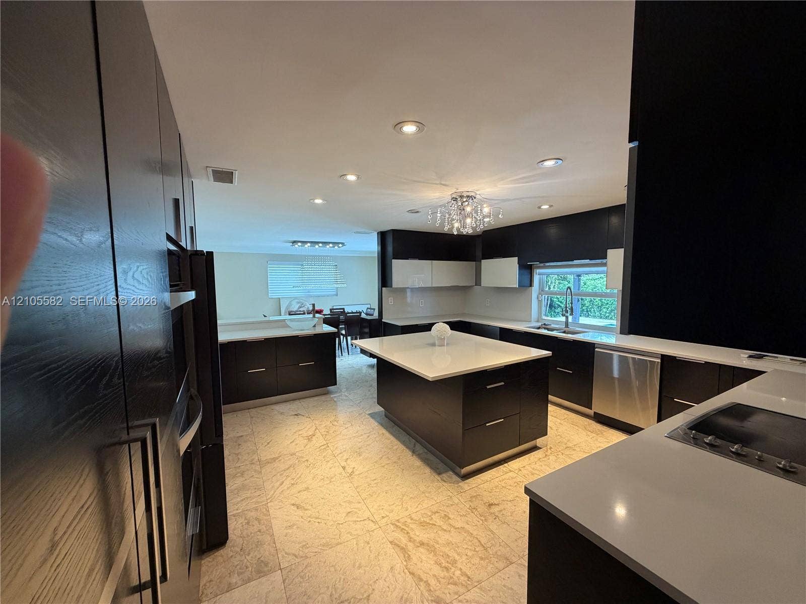 2215 NE 204th Street, Miami, Miami, FL 33180 Gourmet kitchen featuring a large central island, light-toned stone tile flooring, sleek dark cabinetry, and white countertops