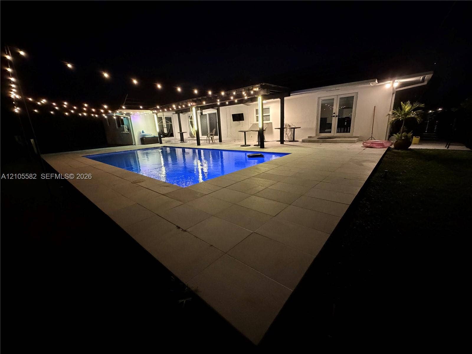 2215 NE 204th Street, Miami, Miami, FL 33180 In-ground pool surrounded by a large paver patio, featuring string lighting and a covered pergola