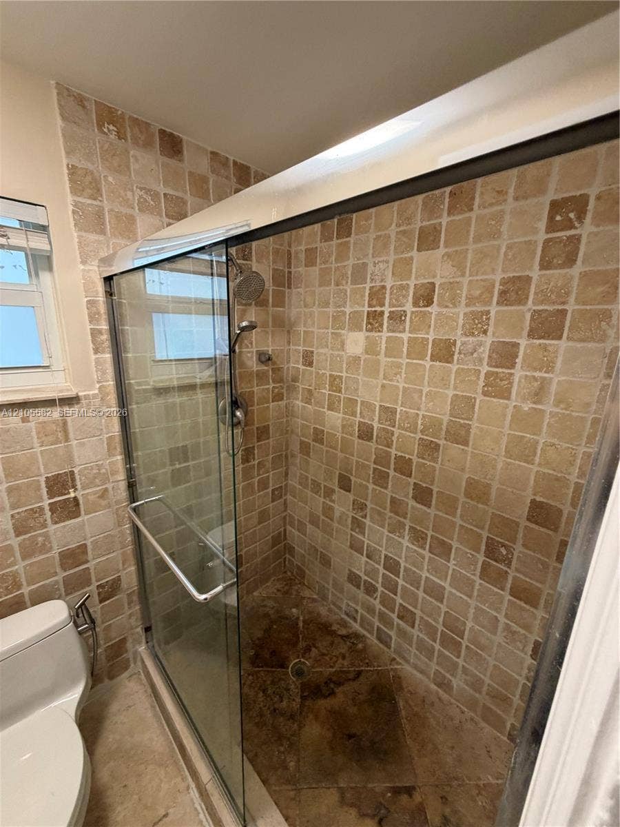 2215 NE 204th Street, Miami, Miami, FL 33180 Enclosed shower with tiled walls and floor, featuring a glass sliding door and a shower head with an attached sprayer