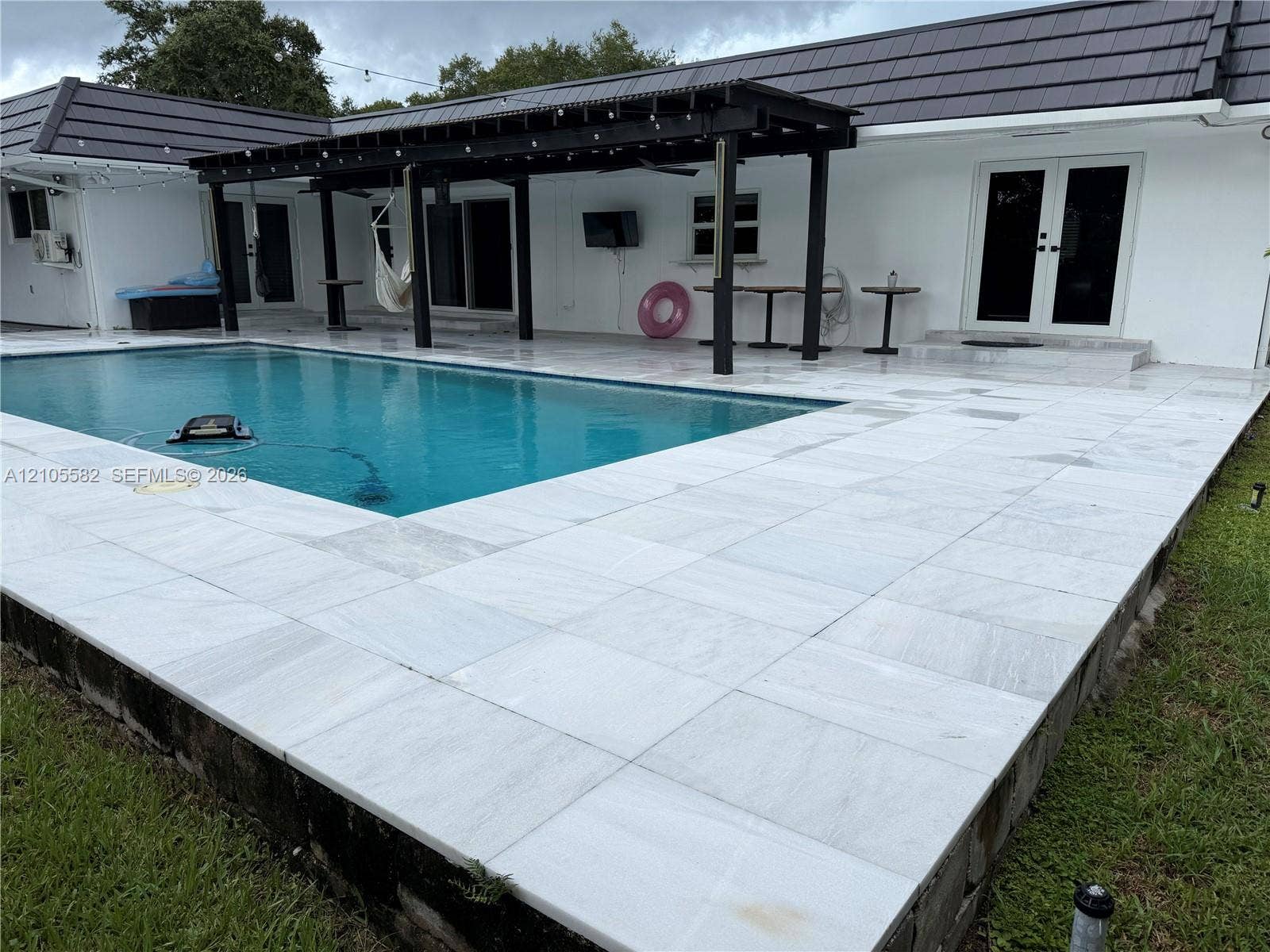 2215 NE 204th Street, Miami, Miami, FL 33180 Outdoor swimming pool with a black-framed pergola, white tiled pool deck, and white exterior stucco finish