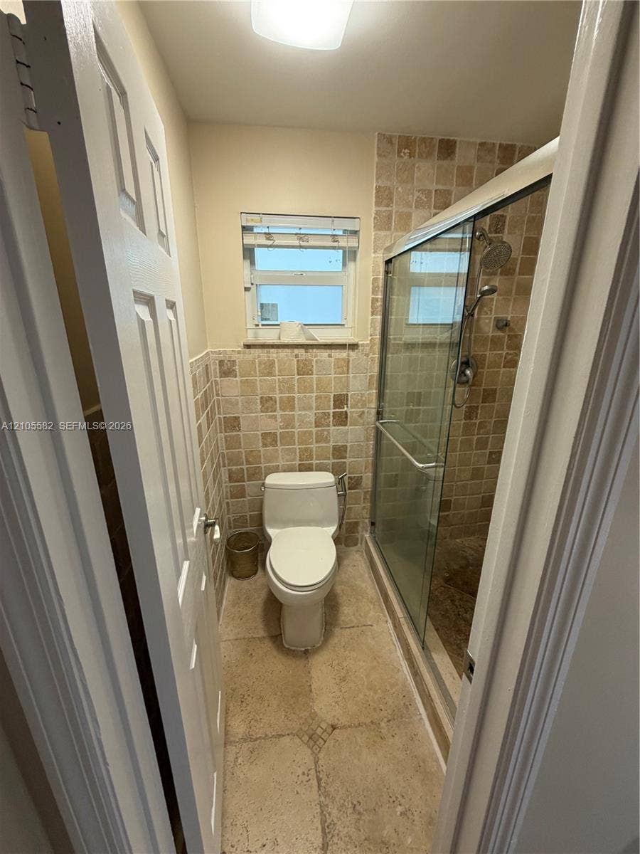 2215 NE 204th Street, Miami, Miami, FL 33180 Tiled shower enclosure with a glass door, wall-mounted showerhead, and a window for natural light