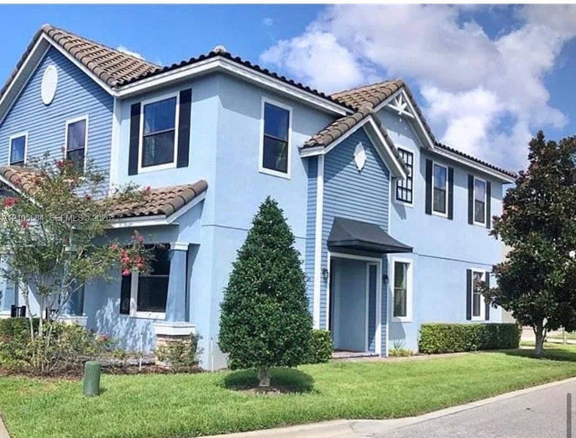 10197 Eagle Creek Center Boulevard, Orlando, FL 32832 Two-story exterior featuring a mix of stucco and horizontal siding, a tiled roof, decorative window shutters, and an arched entryway with a metal awning