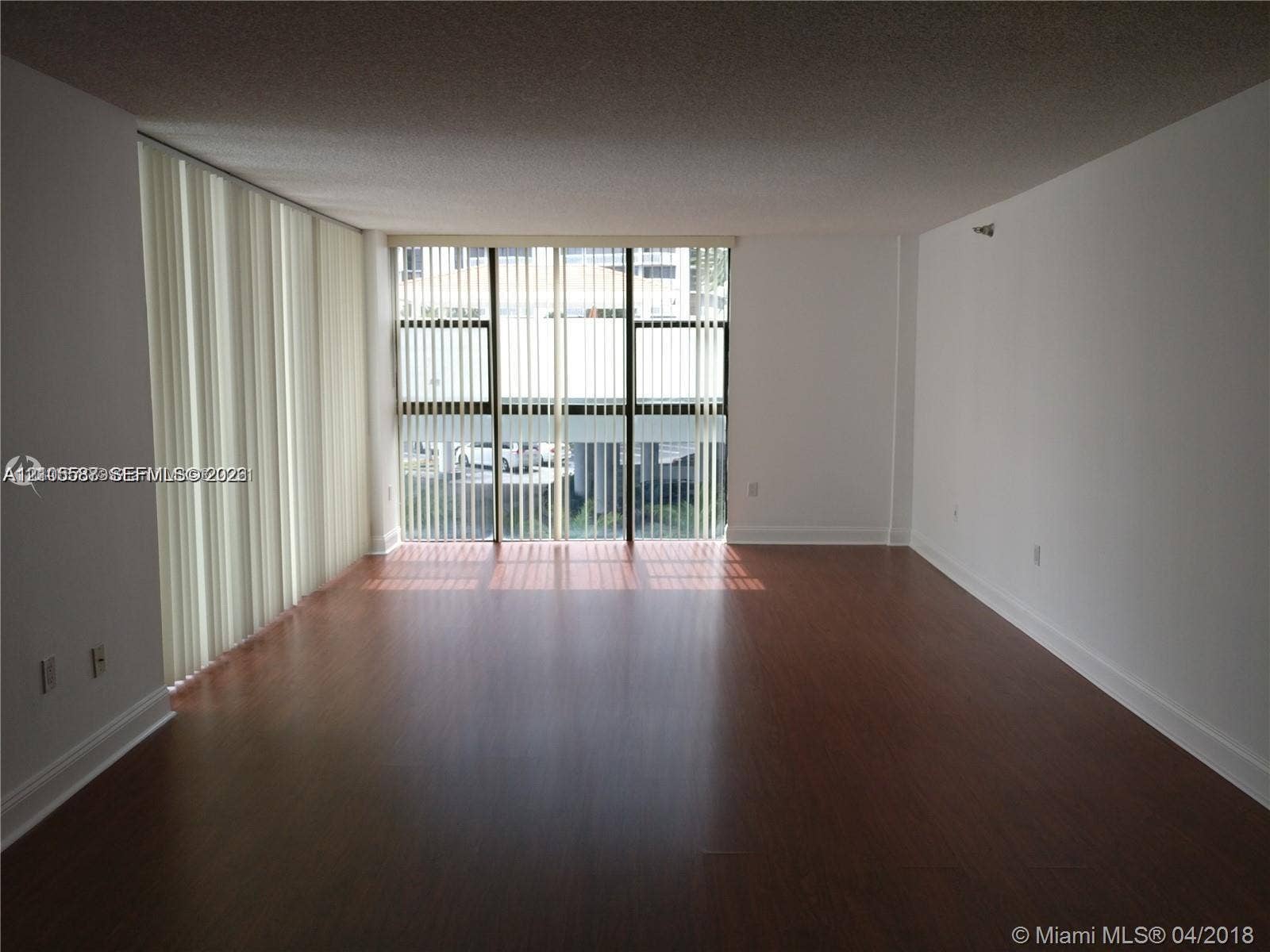Expansive room featuring wood-finish flooring, white walls, and vertical blinds covering a large window