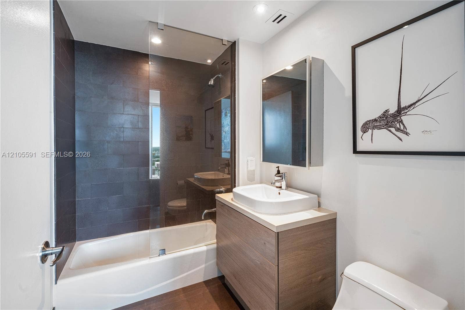 Full bathroom featuring a shower-tub combination with a glass enclosure, dark tile surround, and a compact window