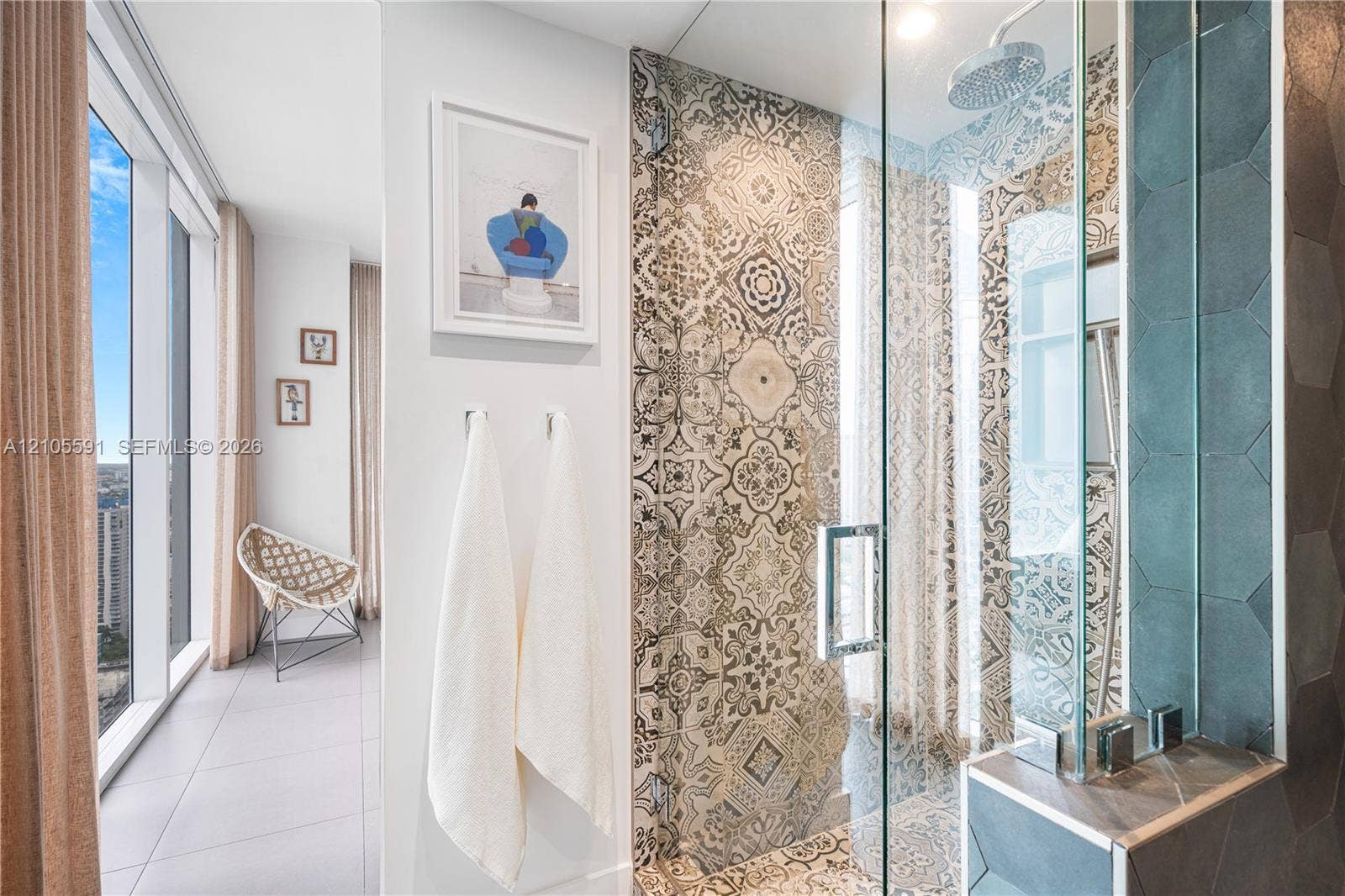 Full-height window with city backdrop, glass shower enclosure, decorative patterned wall tile, rainfall showerhead, and a built-in shower niche