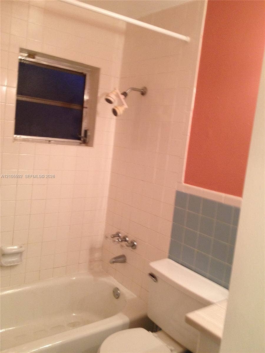White tiled shower surround with a window, white bathtub, and toilet with a tiled wall accent