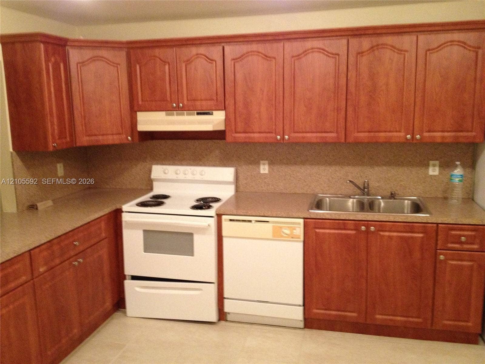 U-shaped kitchen with wood-finish cabinetry, solid surface countertops, a double basin stainless steel sink, and a white electric range