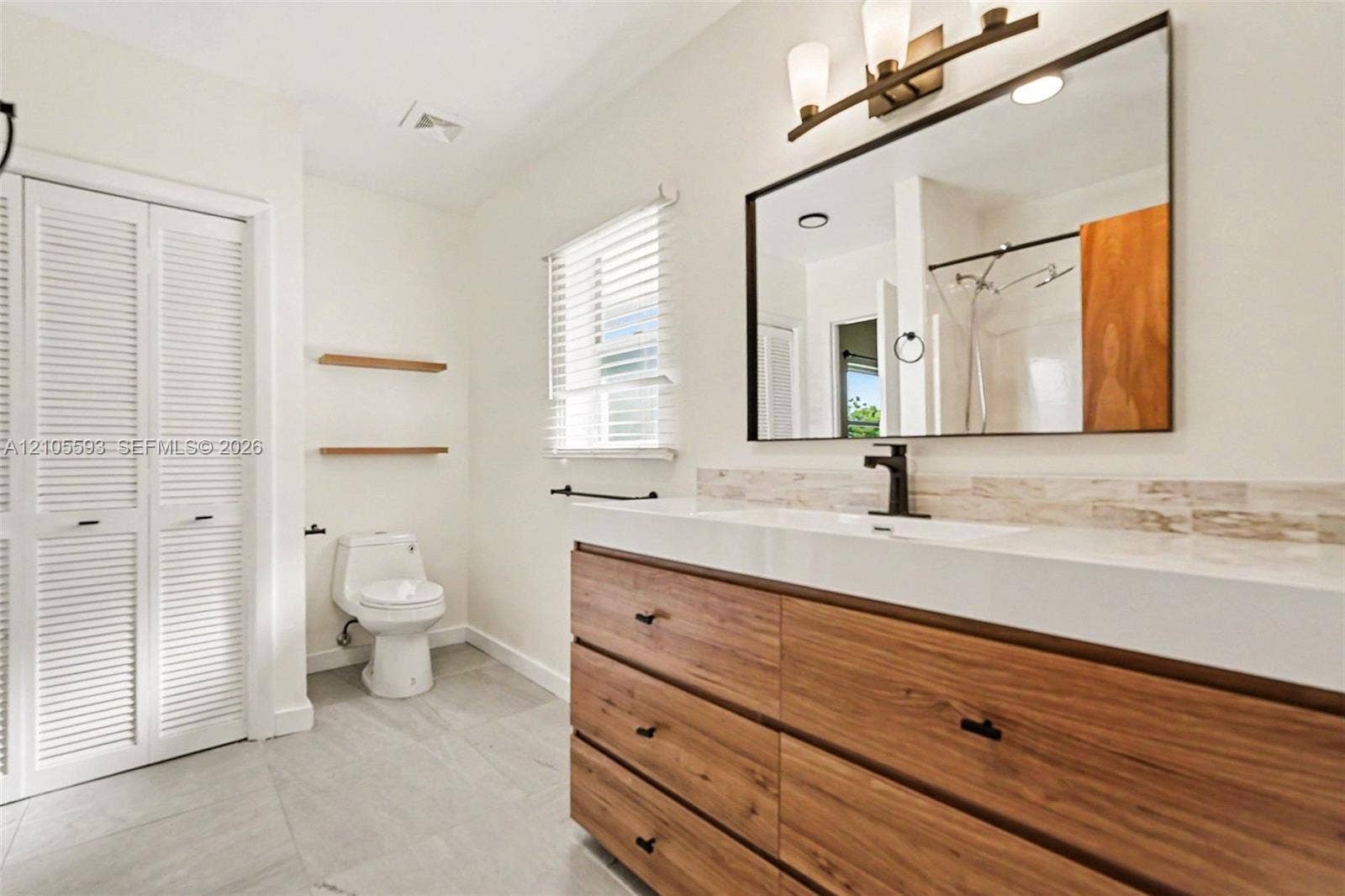 597 Grace Street, Sebastian, FL 32958 Bathroom featuring a wood-finish vanity with a rectangular sink, matte black faucet, framed mirror, and tile flooring