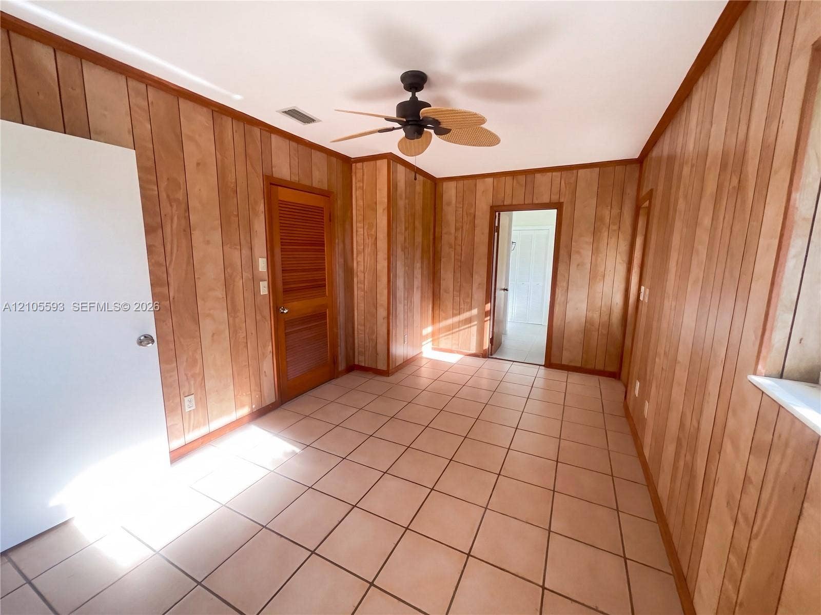 597 Grace Street, Sebastian, FL 32958 Interior room featuring wood-paneled walls, tile flooring, a louvered closet door, and a ceiling fan with integrated lighting