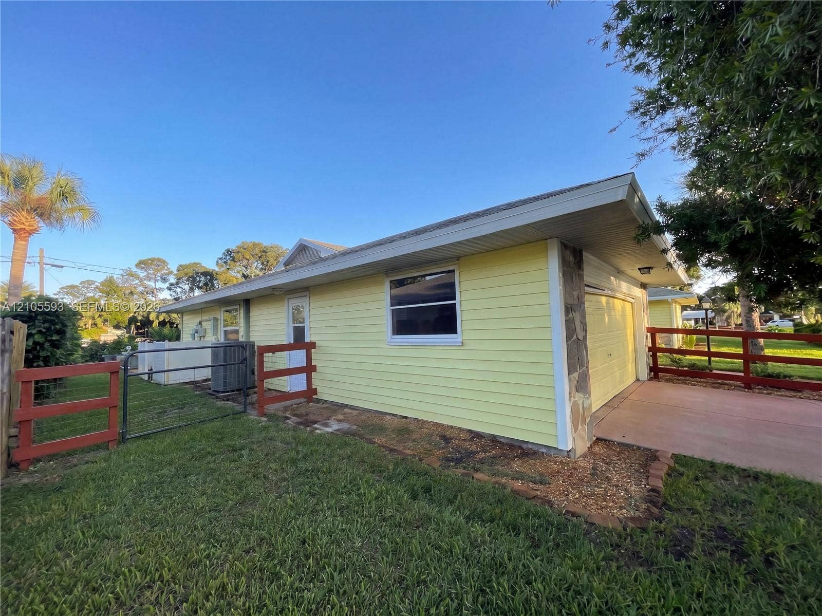 597 Grace Street, Sebastian, FL 32958 Exterior featuring yellow lap siding, stone masonry accents, a concrete driveway, and red-painted wooden post-and-rail fencing