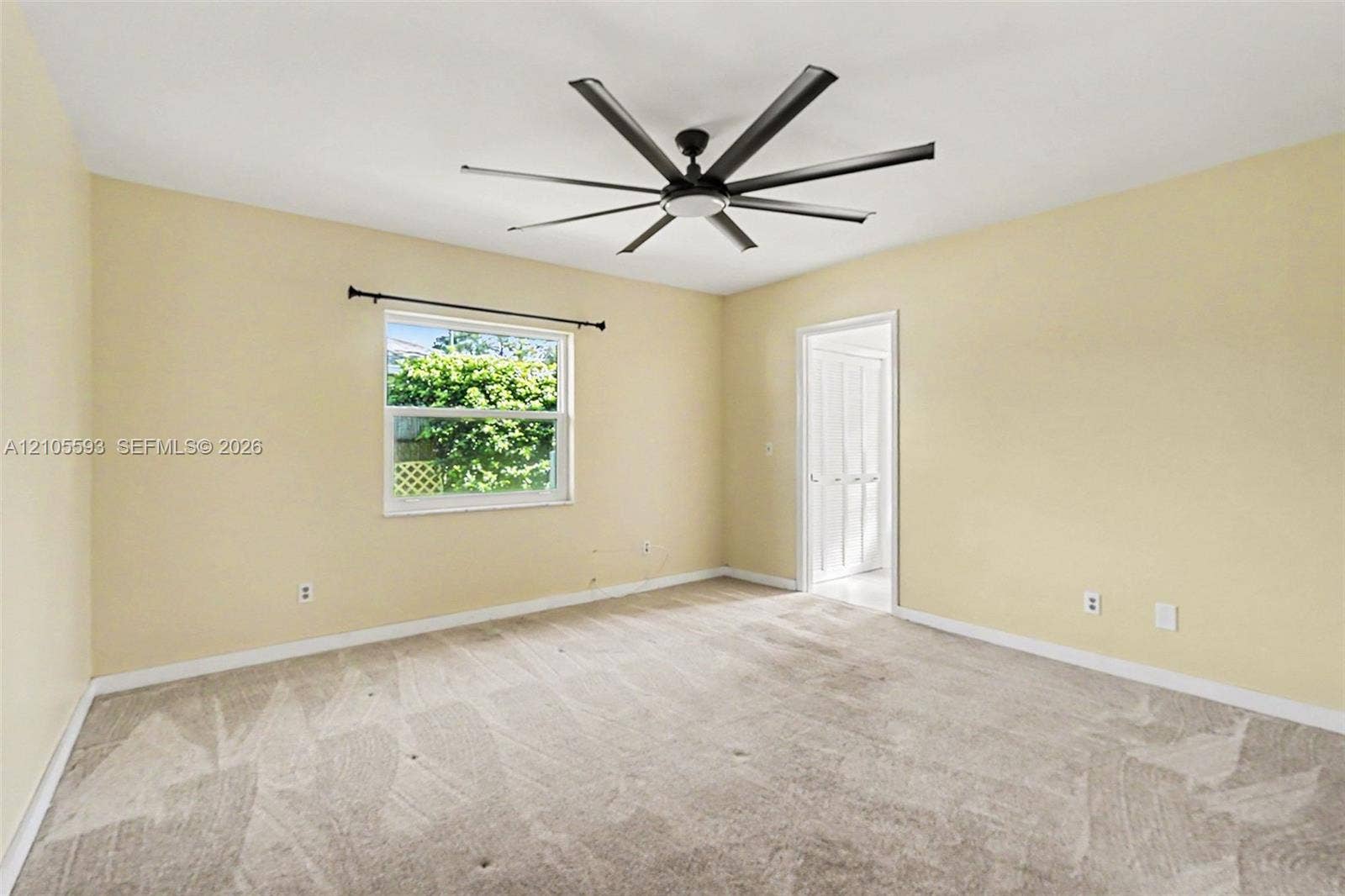 597 Grace Street, Sebastian, FL 32958 Neutral-toned interior room featuring wall-to-wall carpeting, an oversized multi-blade ceiling fan, and a single-pane window with a curtain rod