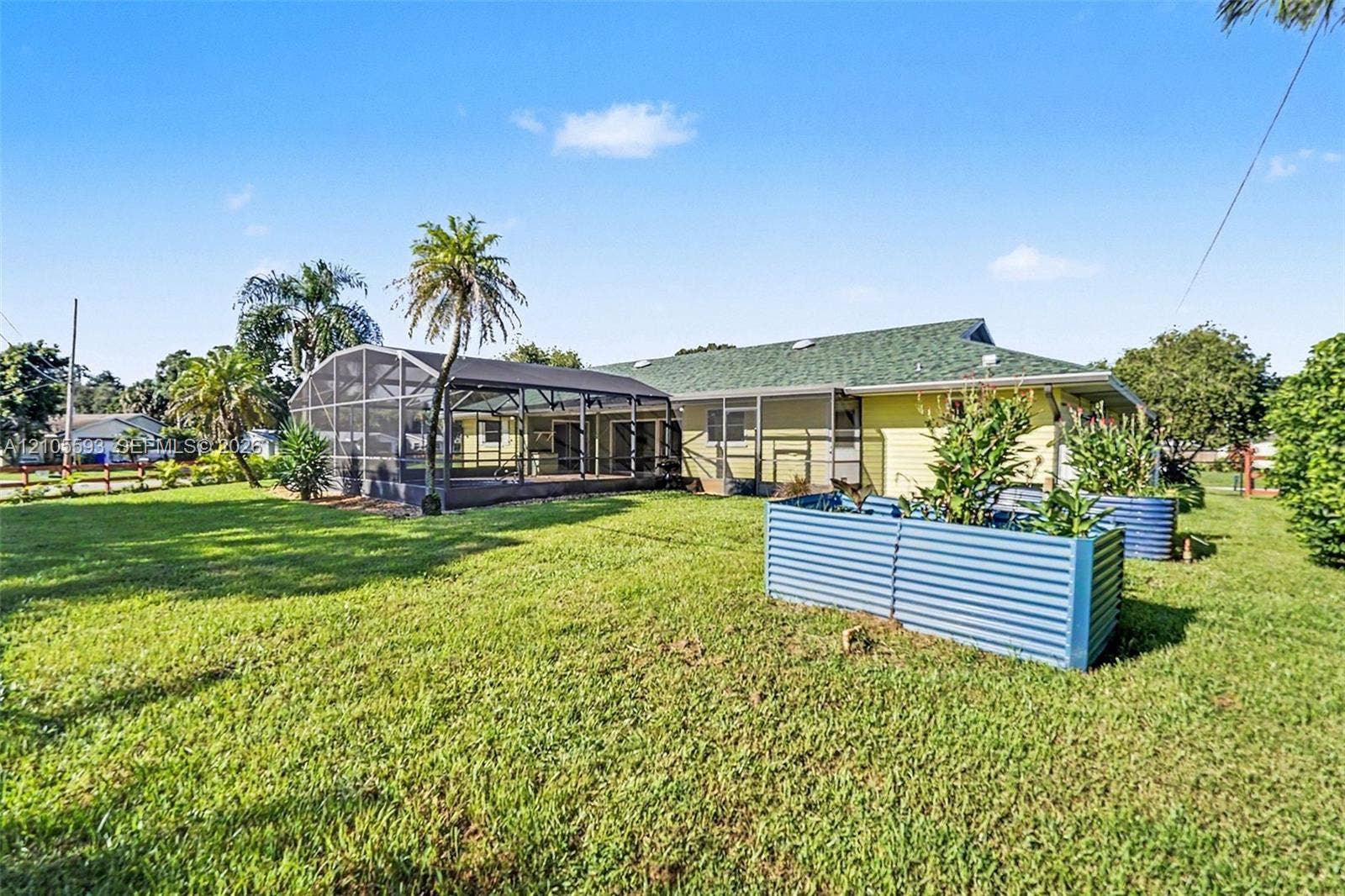 597 Grace Street, Sebastian, FL 32958 Backyard featuring a screened-in lanai, corrugated metal raised garden beds, expansive grass lawn, and mature palm trees