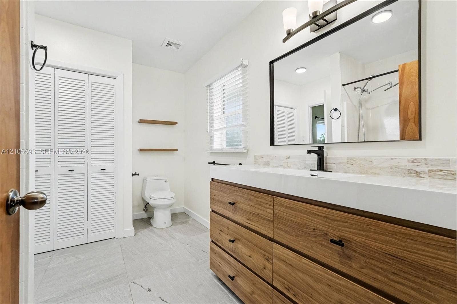 597 Grace Street, Sebastian, FL 32958 Bathroom featuring a wood-finish vanity with a rectangular sink, matte black faucet, wall-mounted mirror, and tile flooring