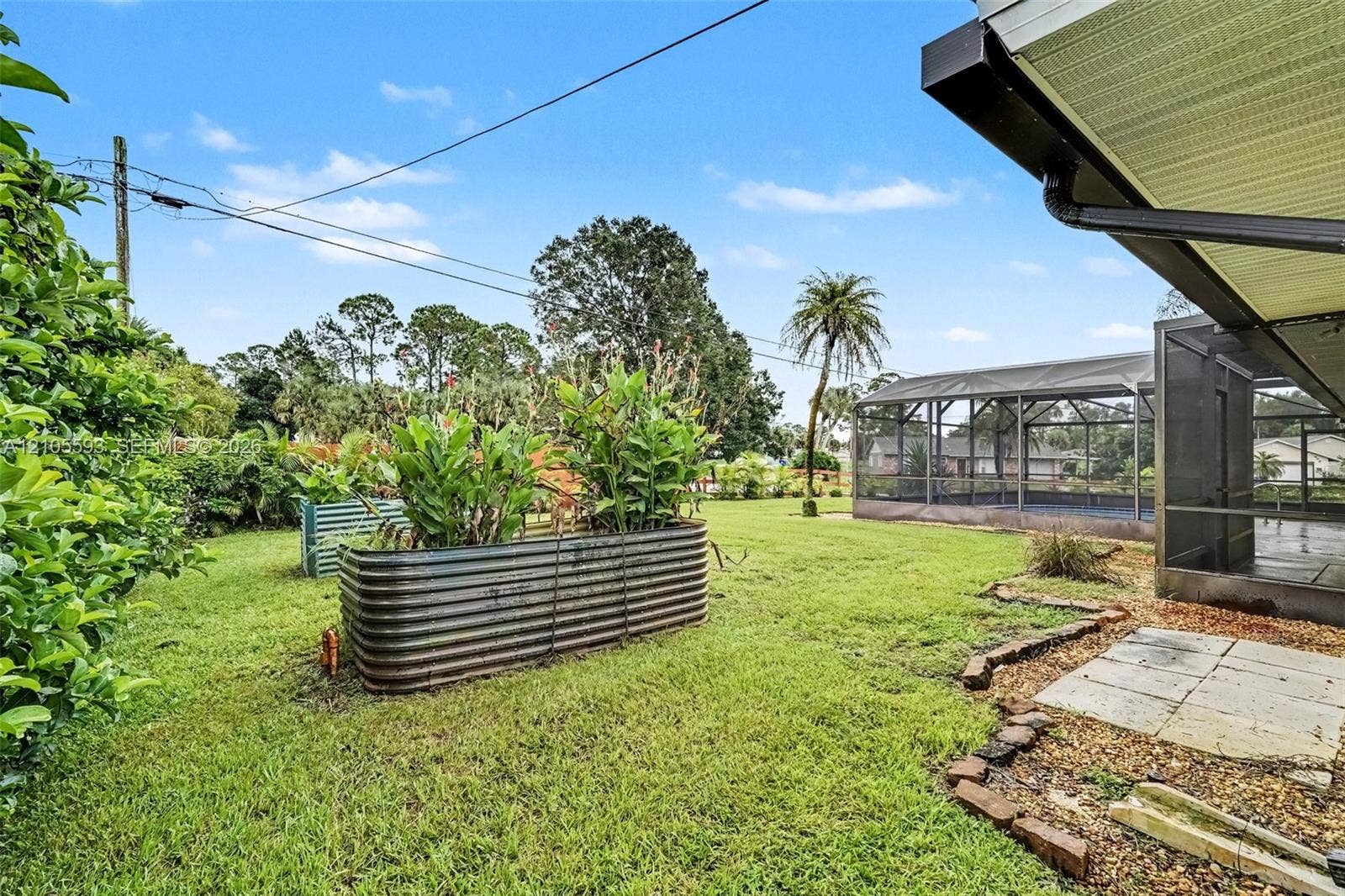 597 Grace Street, Sebastian, FL 32958 Backyard featuring a screened-in lanai, corrugated metal raised garden beds, stone paver patio area, and mature landscaping