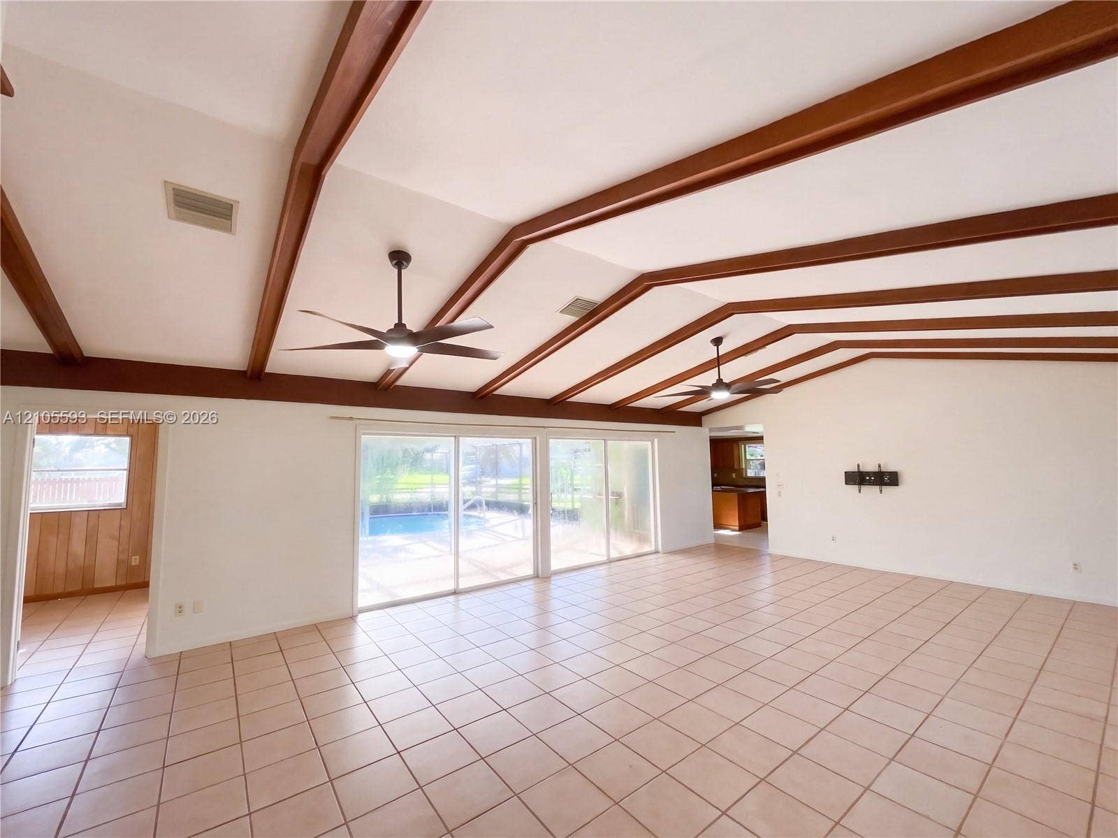 597 Grace Street, Sebastian, FL 32958 Vaulted ceiling with exposed wood beams, neutral tile flooring, dual ceiling fans with integrated lighting, and glass sliding doors