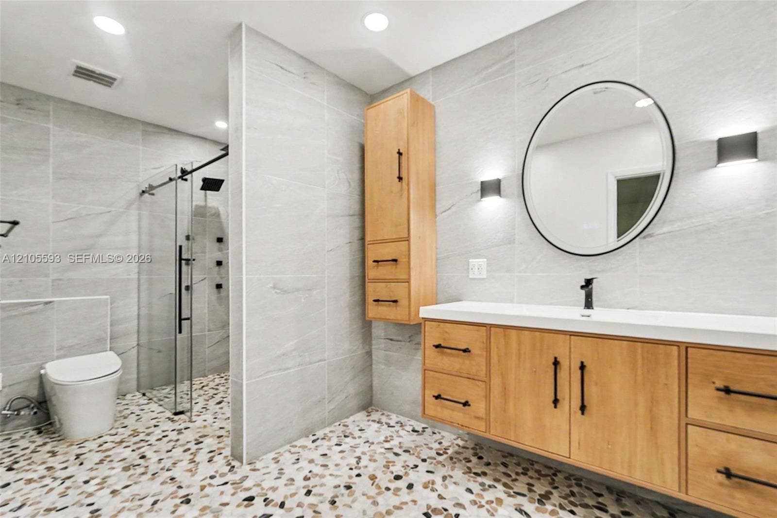 597 Grace Street, Sebastian, FL 32958 Bathroom featuring a floating vanity with wood-finish cabinetry, a white countertop, a walk-in shower with a glass enclosure, wall-to-wall stone-tiled surfaces, and river-stone flooring