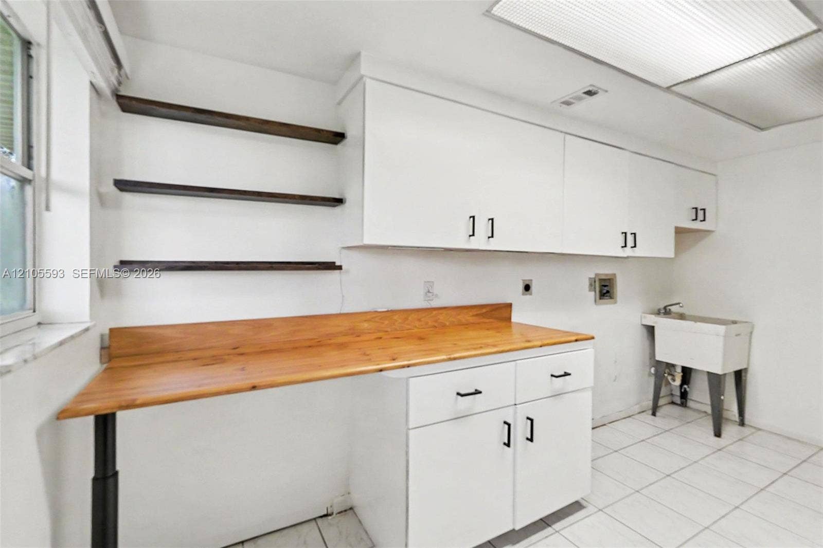 597 Grace Street, Sebastian, FL 32958 Laundry area featuring white cabinetry, a wood-finish countertop workspace, open shelving, a utility sink, and tile flooring