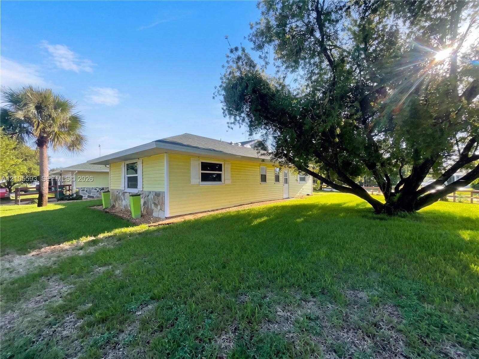 597 Grace Street, Sebastian, FL 32958 Exterior featuring yellow horizontal siding, stone veneer accents, a low-pitch roof, and a large, established tree on the lawn