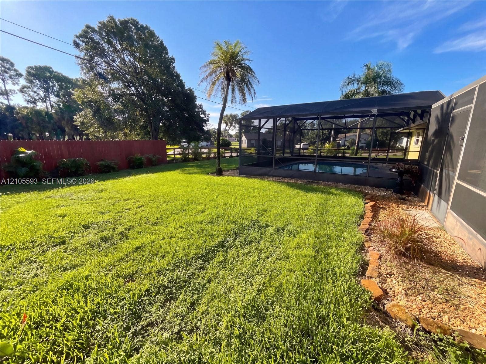 597 Grace Street, Sebastian, FL 32958 Backyard featuring a screened-in pool enclosure, stone-border landscaping, and a fenced perimeter