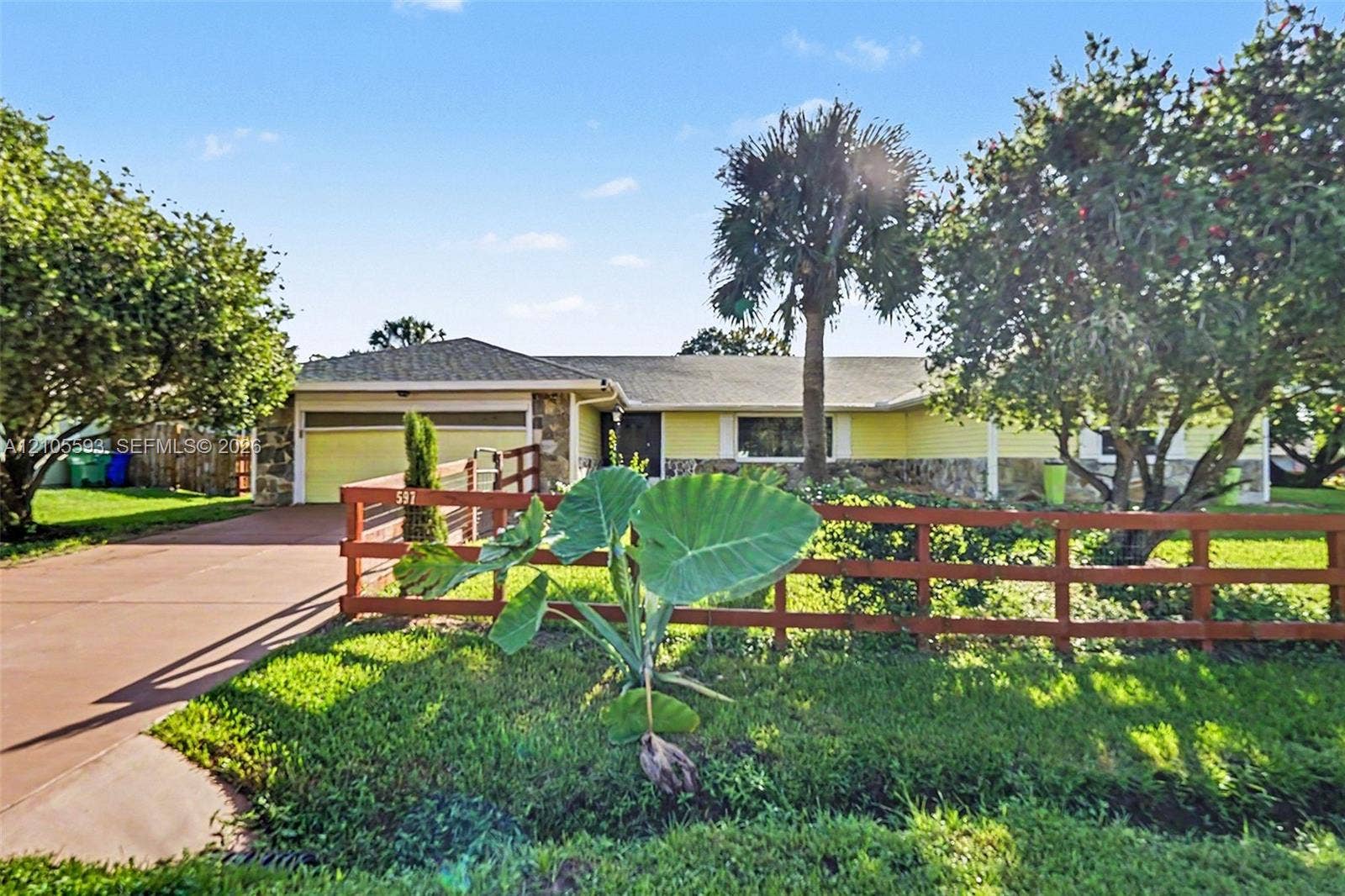 597 Grace Street, Sebastian, FL 32958 Rambling-style exterior featuring stone masonry accents, horizontal siding, a two-car garage, and post-and-rail perimeter fencing